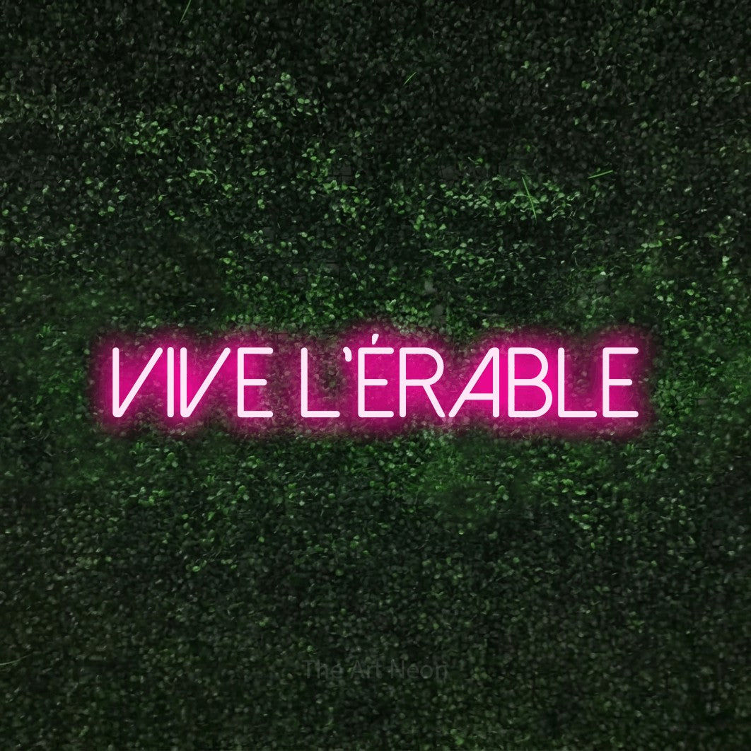 “Vive l'érable” LED neon sign in hot pink, with thin sans-serif lettering, shown against a textured green hedge.
