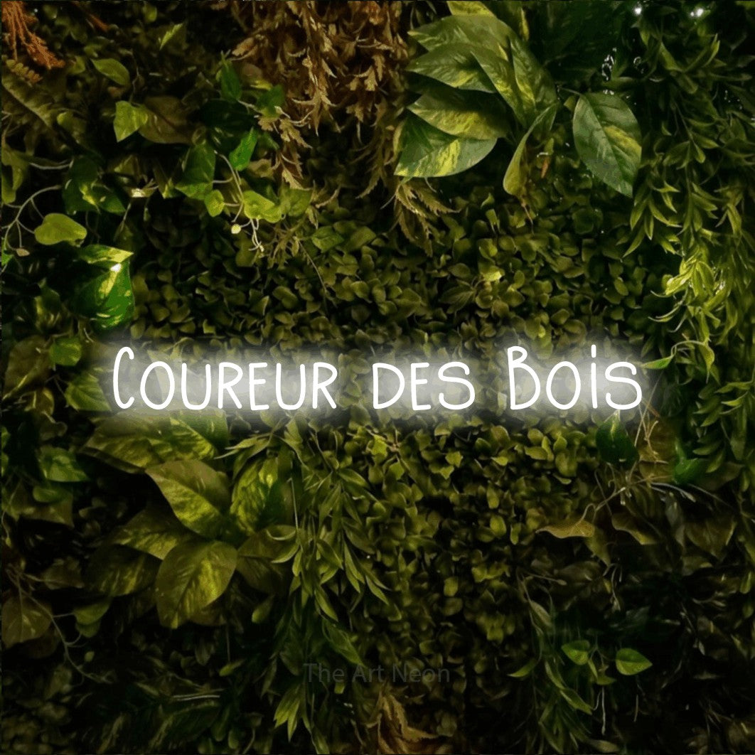 “Coureur des bois” LED neon sign in cool white, with narrow hand-drawn lettering, shown against bright green and yellow foliage.