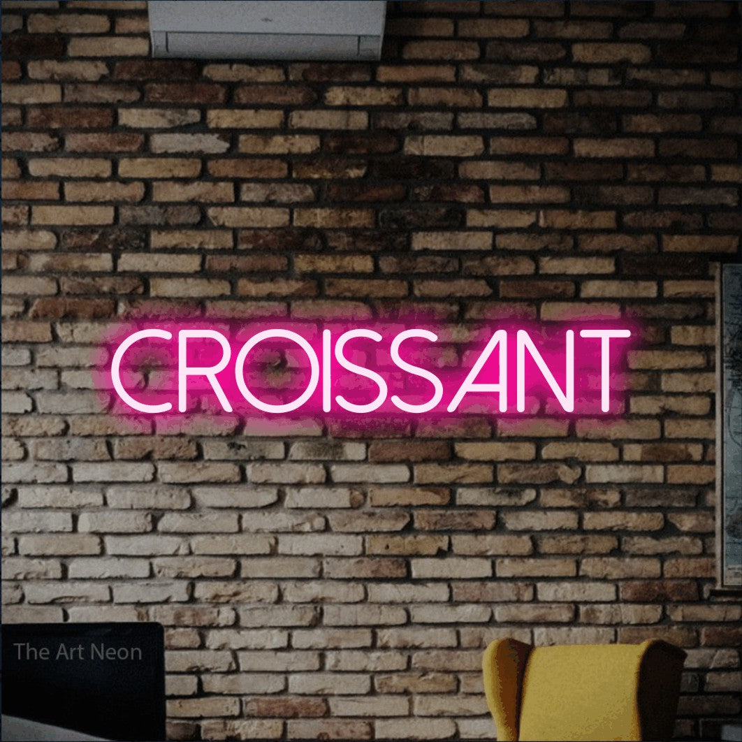 “Croissant” LED neon sign in hot pink, with thin sans-serif lettering, shown against warm-toned brickwork.