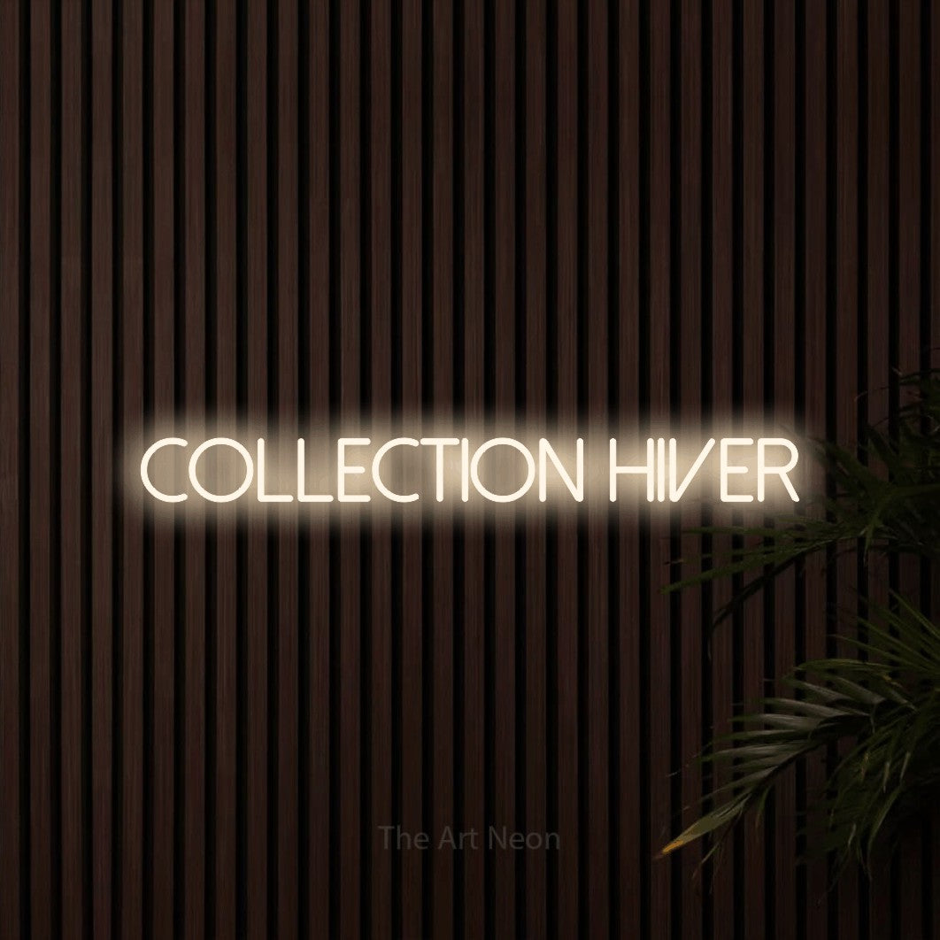“Collection hiver” LED neon sign in warm white, with thin sans-serif lettering, shown against dark wooden wall slats.