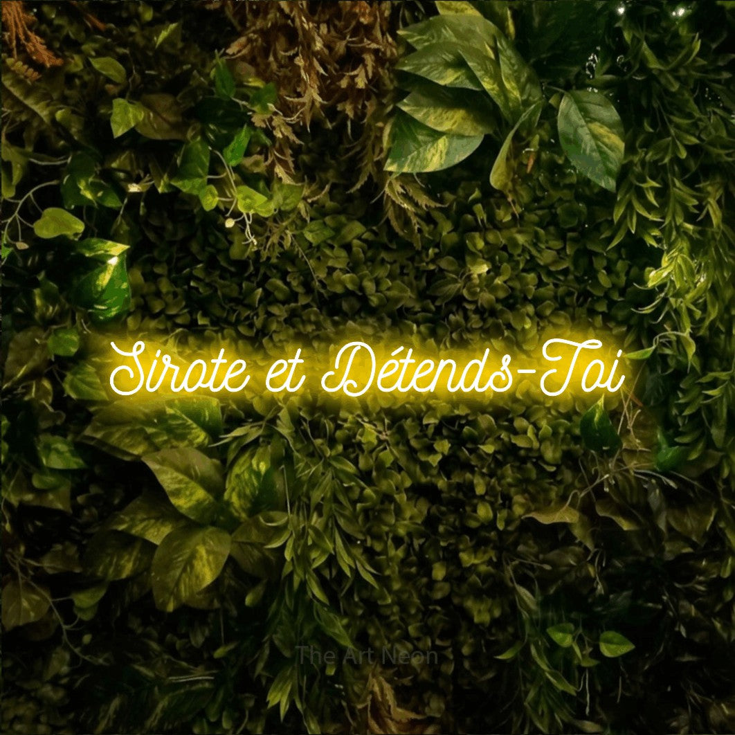 Enseigne néon LED « Sirote et détends-toi » en jaune, en écriture cursive ornée, présentée sur un feuillage vert et jaune vif, pour un bar à la maison.