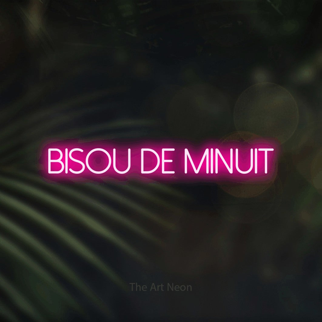 “Bisou de minuit” LED neon sign in hot pink, with thin sans-serif lettering, shown against a blurred palm and bokeh-light backdrop.