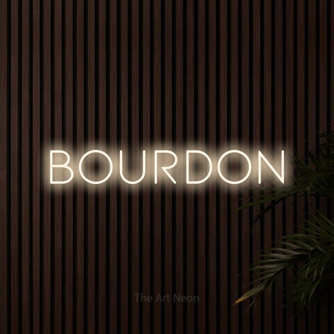 “Bourdon” LED neon sign in warm white, with thin, widely spaced lettering, shown against dark wooden wall slats.