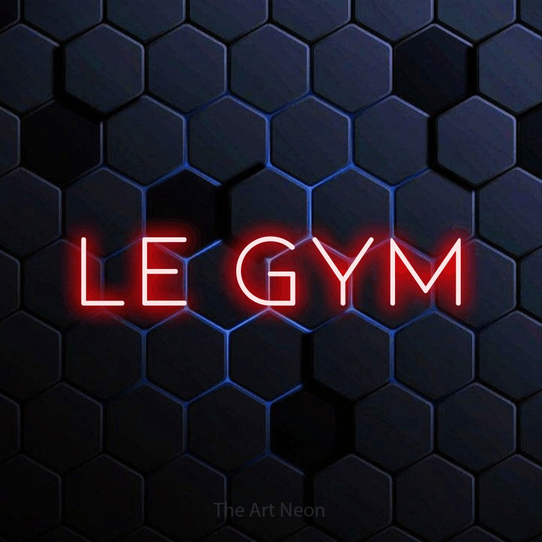 Décoration murale en néon LED « Le gym » en rouge, en lettres fines et espacées, installée sur un motif alvéolé bleu foncé, pour un espace d’entraînement.