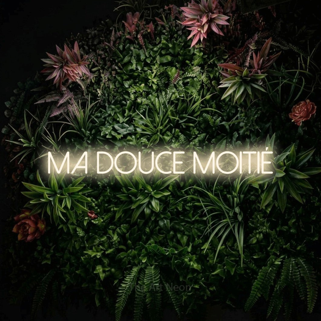 Décoration murale en néon LED « Ma douce moitié » en blanc chaud, en lettres fines sans empattement, installée sur un mur végétal fleuri, pour un décor romantique.