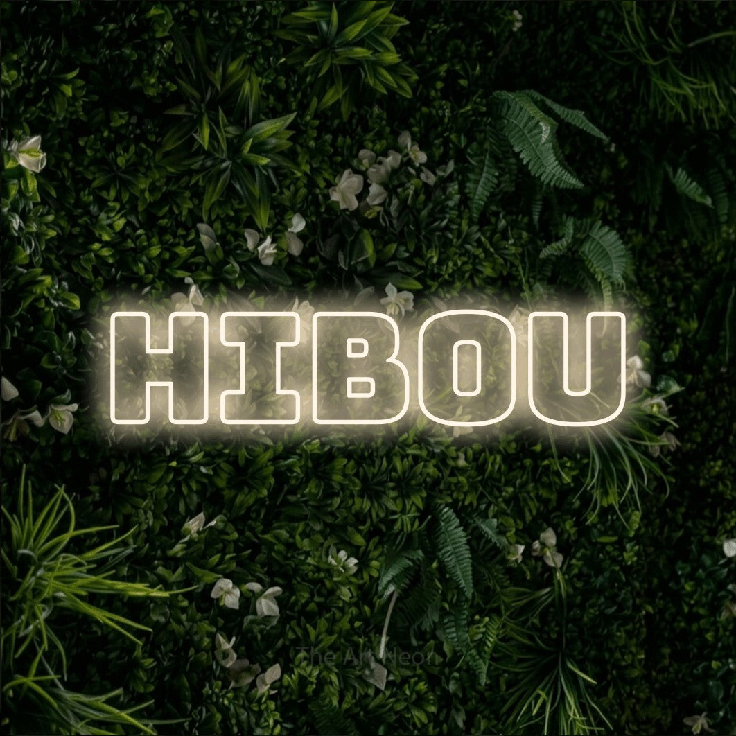 Lettrage en néon LED « Hibou » en blanc chaud, en typographie contour épaisse, présenté sur un mur végétal vert et dense, pour un décor inspiré de la nature.