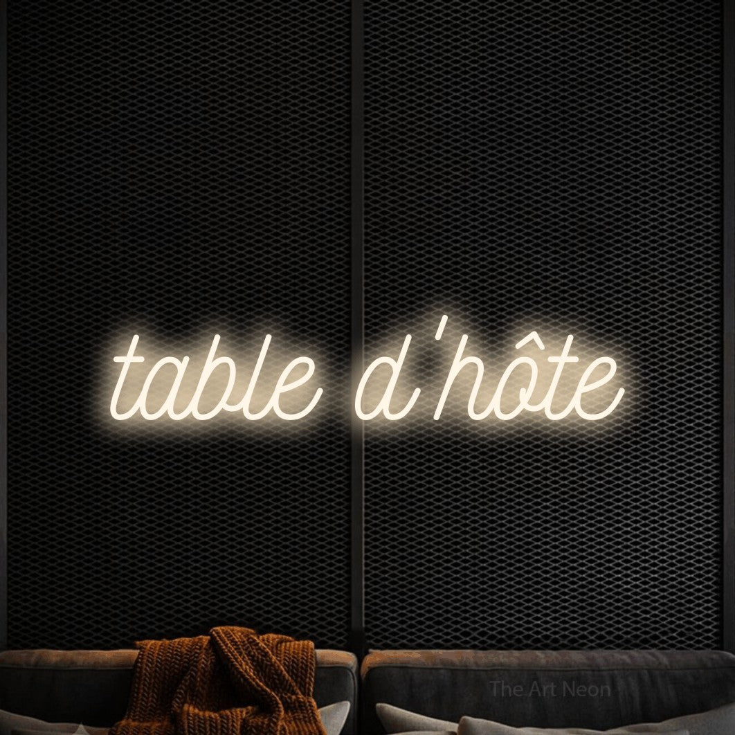 “Table d'hôte” LED neon sign in warm white, with ornate cursive lettering, shown against a modern dark-toned seating area.