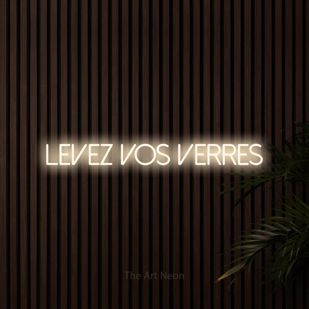 Décoration murale en néon LED « Levez vos verres » en blanc chaud, en lettres fines sans empattement, installée sur un mur de lattes en bois foncé, pour un bar ou un pub.