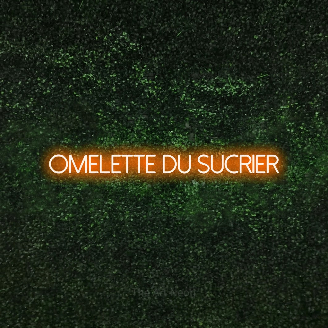 “Omelette du sucrier” LED neon sign in orange, with thin sans-serif lettering, shown against a textured green hedge.