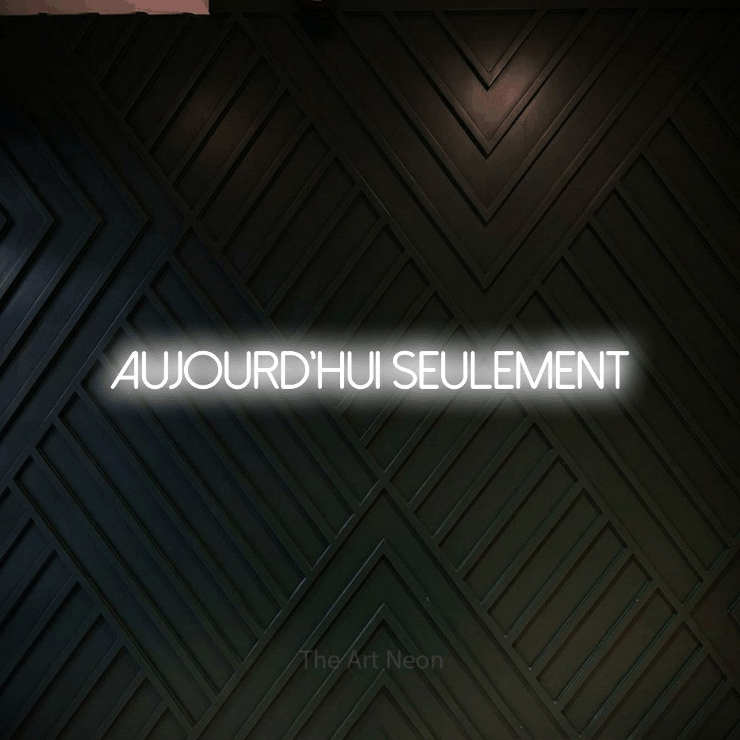 “Aujourd'hui seulement” LED neon sign in cool white, with thin sans-serif lettering, shown against a black chevron-patterned wood wall.