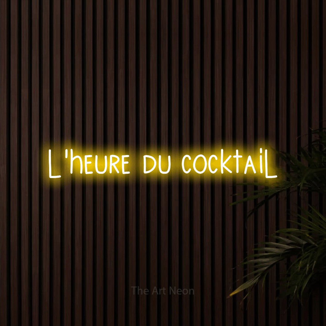 “L'heure du cocktail” LED neon sign in yellow, with narrow hand-drawn lettering, shown against dark wooden wall slats.