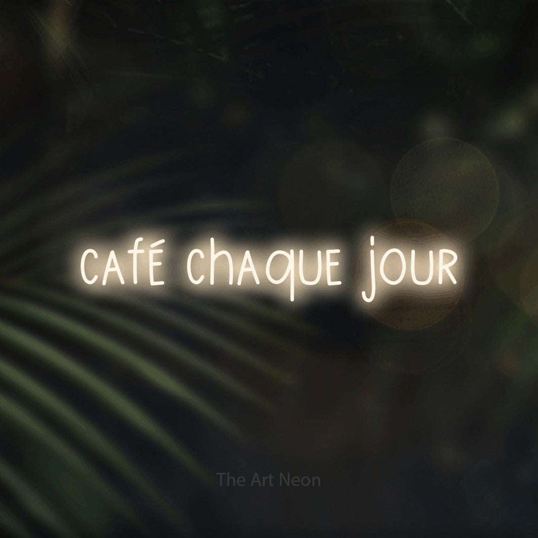 “Café chaque jour” LED neon sign in warm white, with narrow hand-drawn lettering, shown against a blurred palm and bokeh-light backdrop.