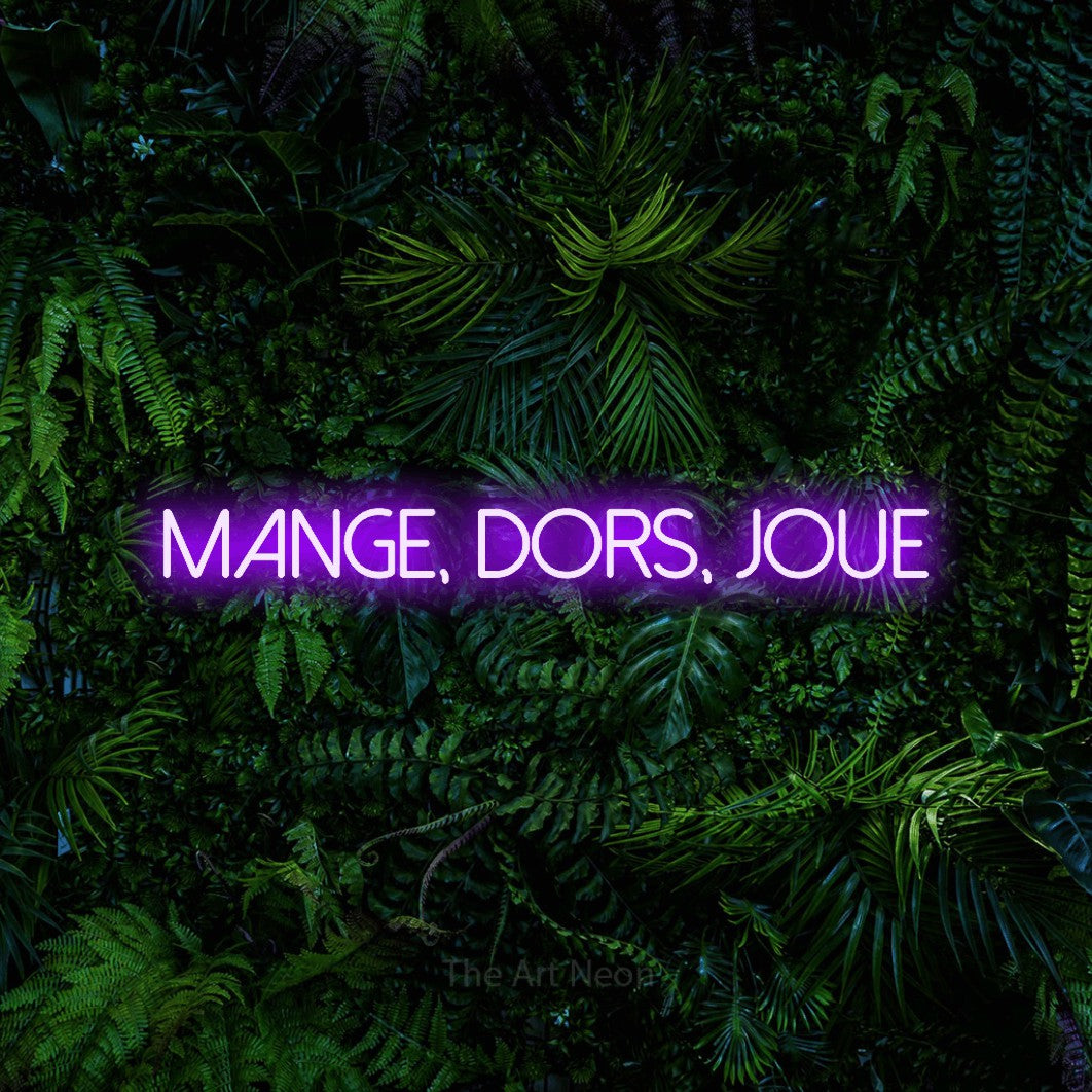 “Mange, dors, joue” LED neon sign in purple, with thin sans-serif lettering, shown against dense tropical foliage.