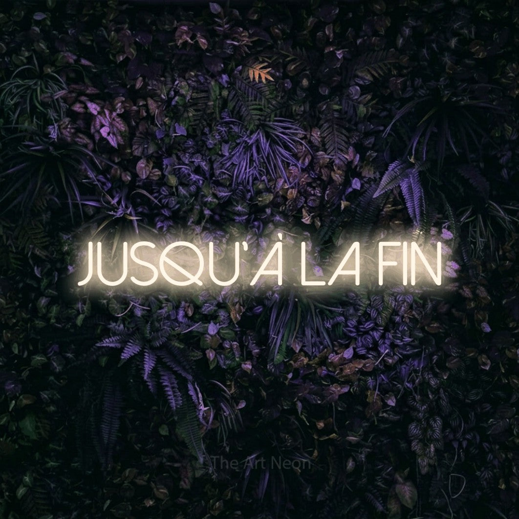 “Jusqu'à la fin” LED neon sign in warm white, with thin sans-serif lettering, shown against a dark wall with purple flowers.