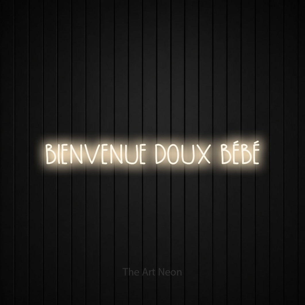 “Bienvenue doux bébé” LED neon sign in warm white, with narrow hand-drawn lettering, shown against black vertical wall slats.
