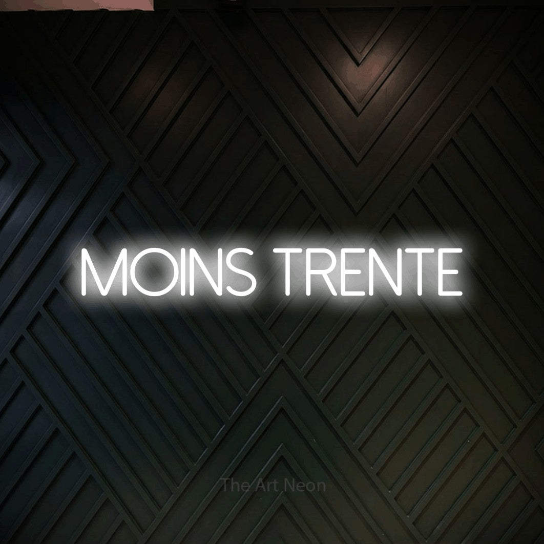 Décoration murale en néon LED « Moins trente » en blanc froid, en lettres fines sans empattement, installée sur un mur en bois noir à motif chevron, pour un décor canadien.