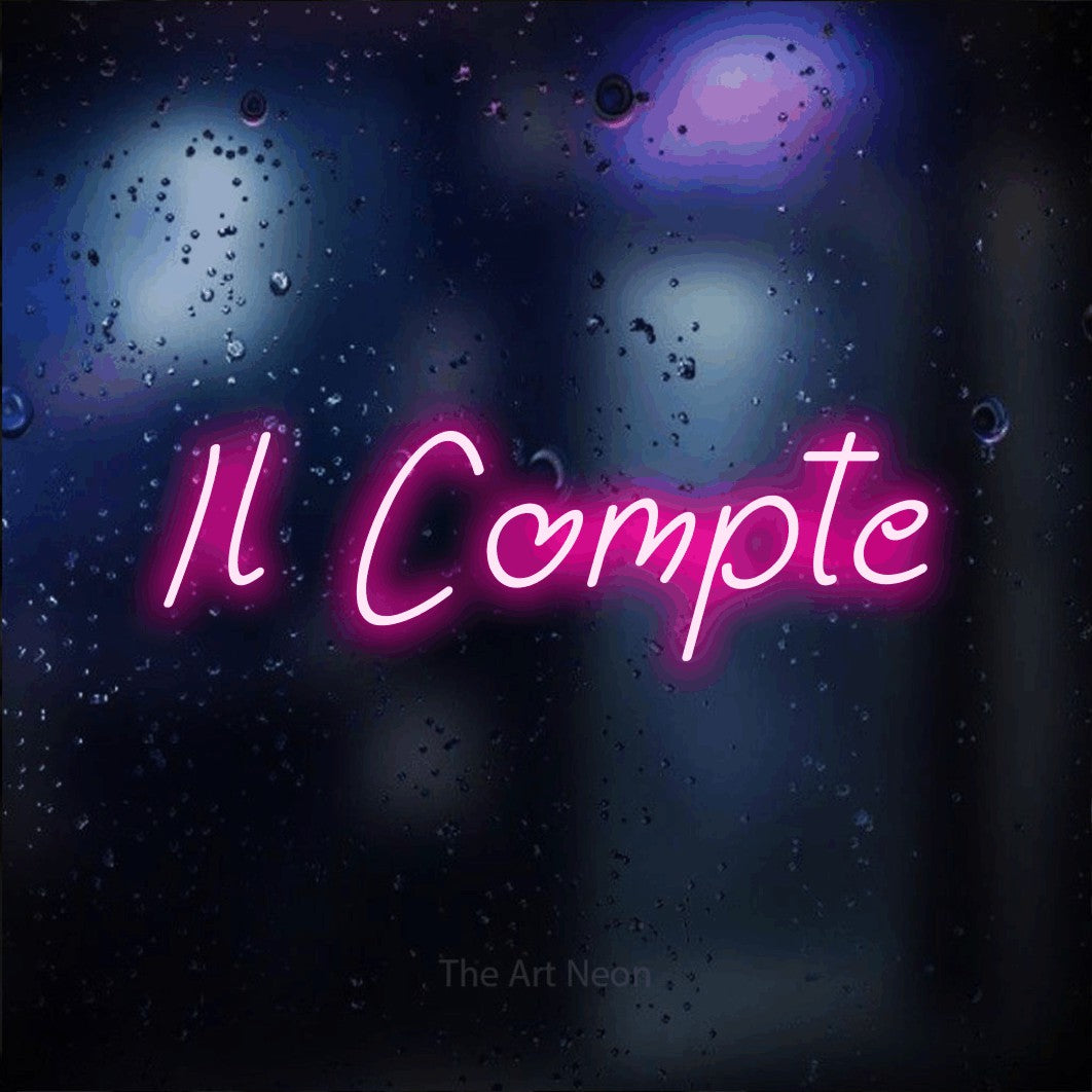 “Il compte” LED neon sign in hot pink, with slanted handwritten lettering, shown against glass with blue and purple reflections.