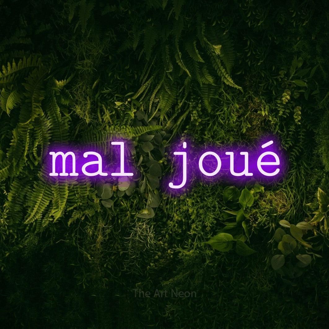 “Mal joué” LED neon sign in purple, with typewriter-style lettering, shown against a dark moss and forest backdrop.