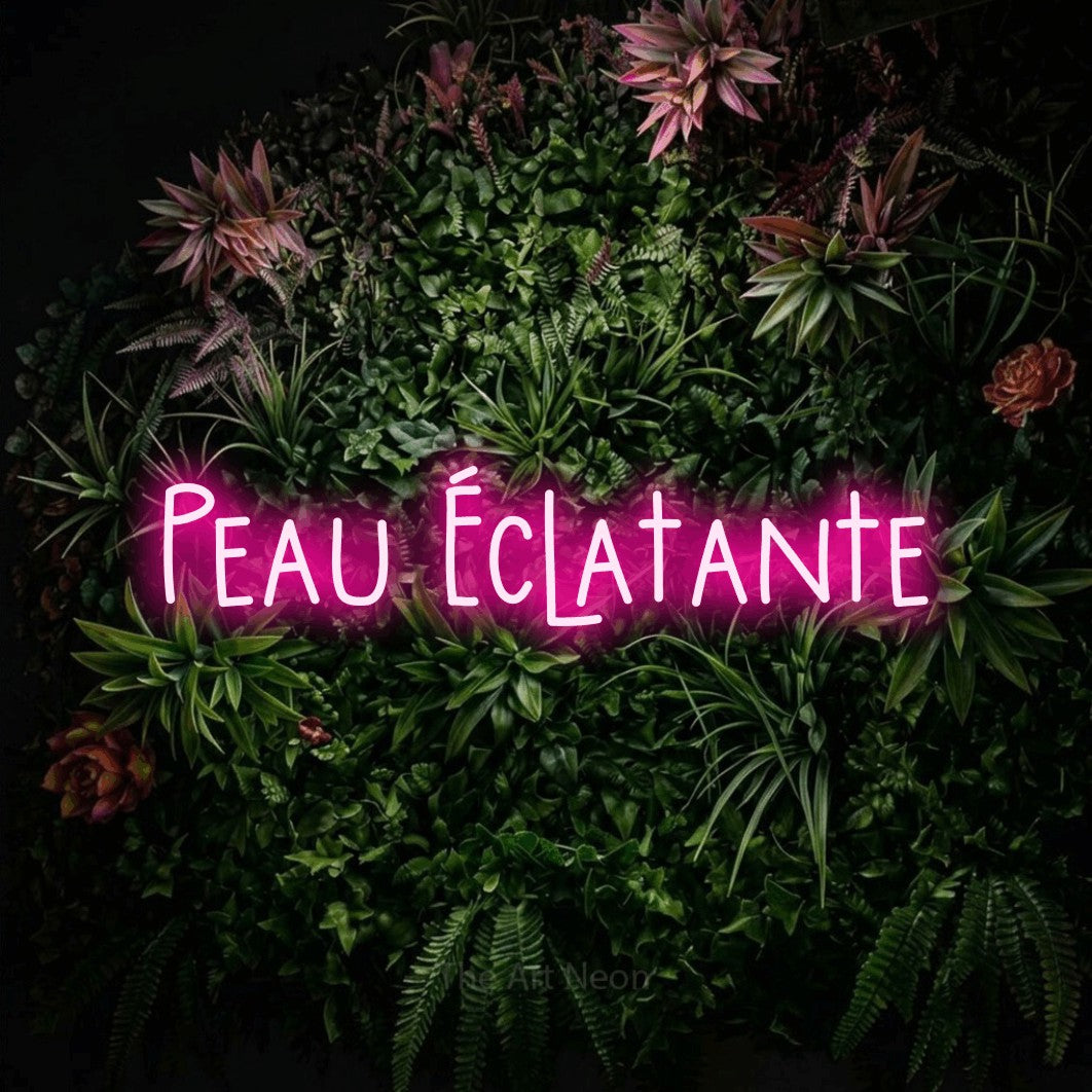 Enseigne néon LED « Peau éclatante » en rose vif, en lettres étroites dessinées à la main, présentée sur un mur végétal fleuri, pour un salon de beauté.