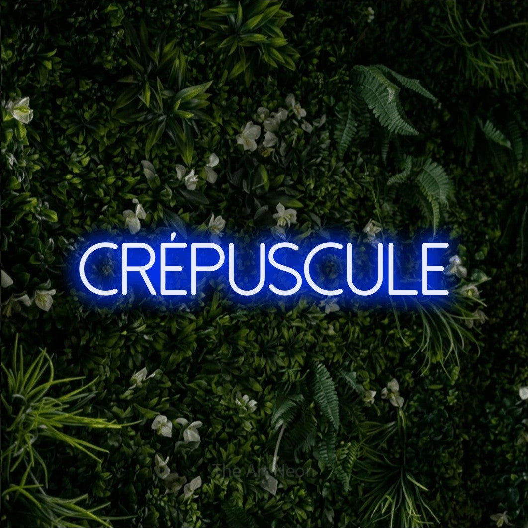 “Crépuscule” LED neon sign in blue, with thin sans-serif lettering, shown against a dense green plant wall.
