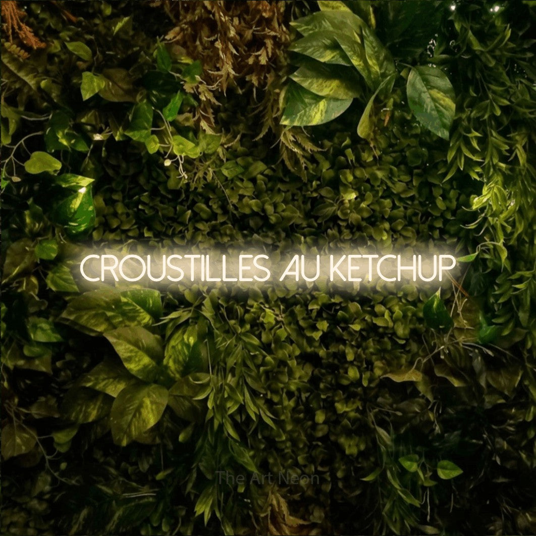 Décoration murale en néon LED « Croustilles au ketchup » en blanc chaud, en lettres fines sans empattement, installée sur un feuillage vert et jaune vif, pour un décor canadien.