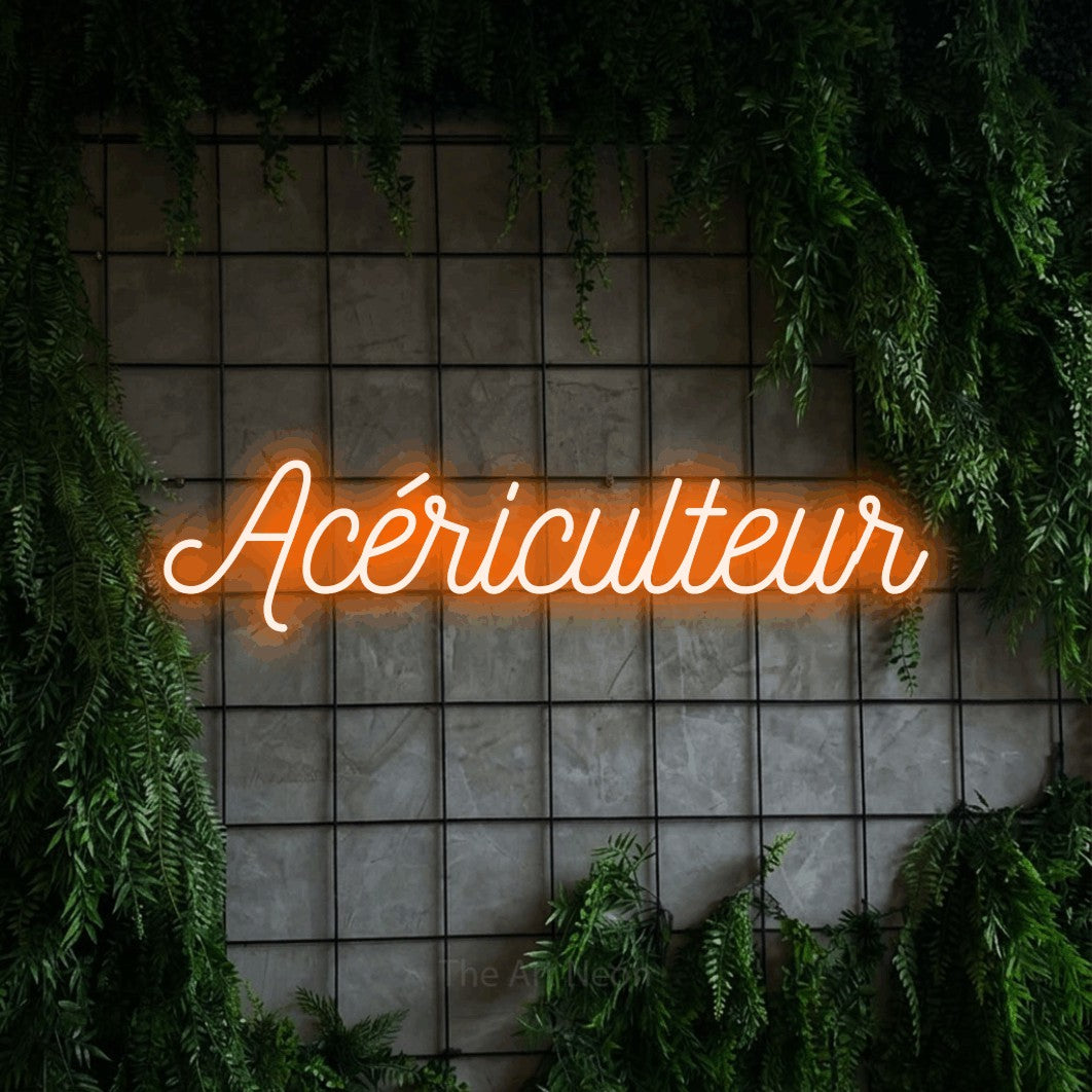 Néon LED « Acériculteur » en orange, en écriture cursive ornée, mis en scène sur une grille de béton couverte de lierre, pour une cabane à sucre.
