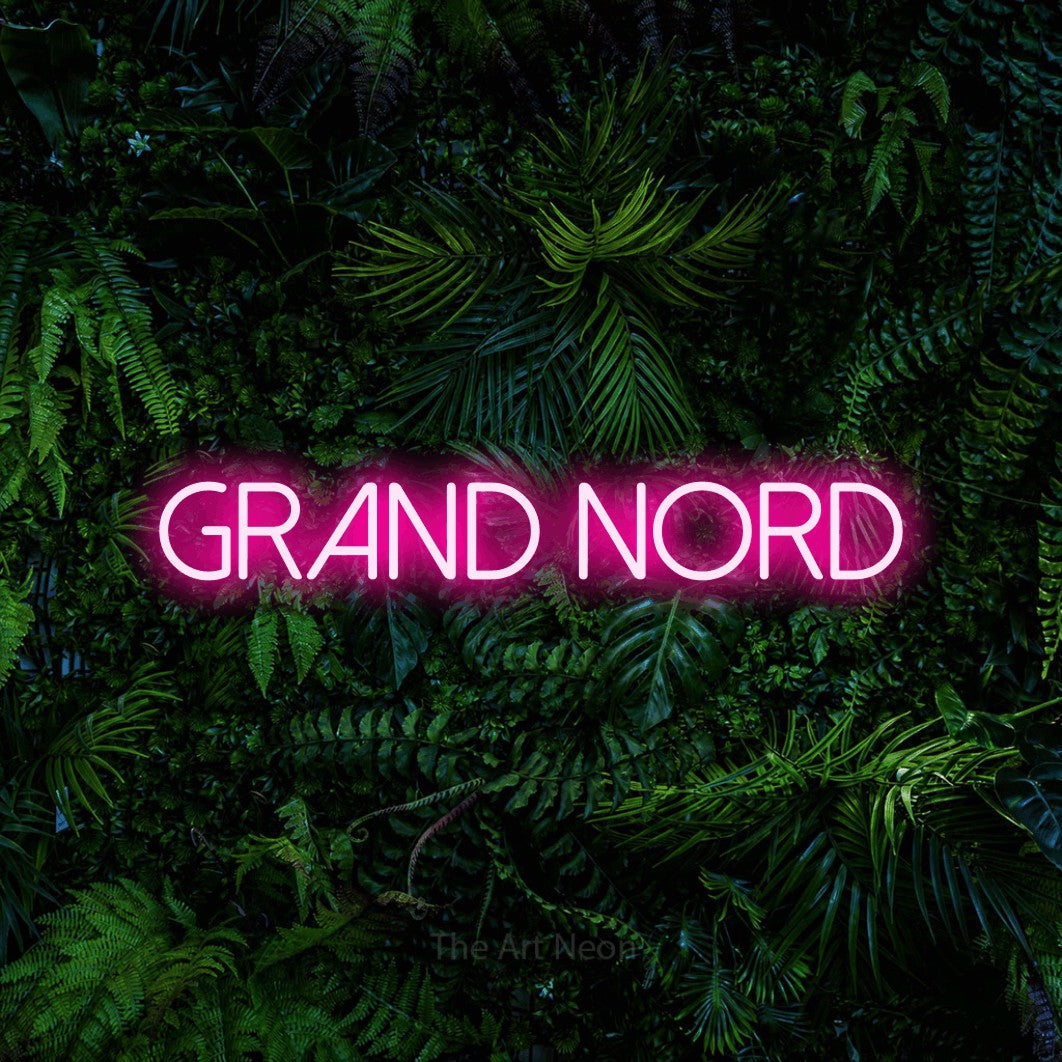 “Grand nord” LED neon sign in hot pink, with thin sans-serif lettering, shown against dense tropical foliage.