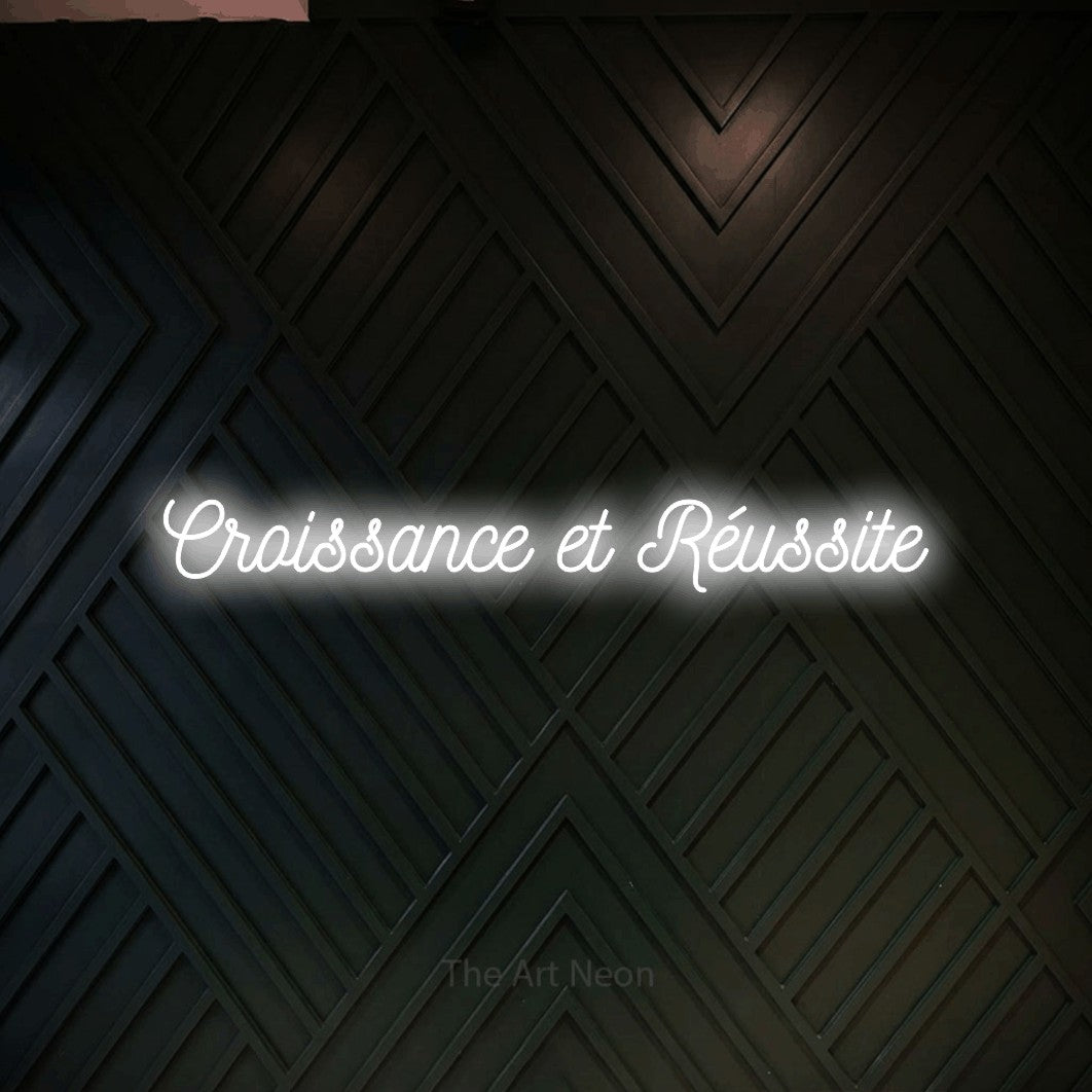 “Croissance et réussite” LED neon sign in cool white, with ornate cursive lettering, shown against a black chevron-patterned wood wall.
