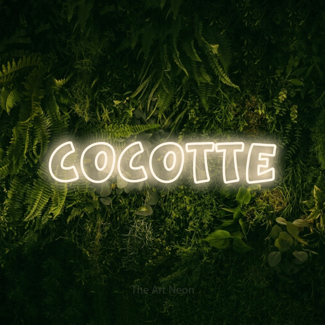 “Cocotte” LED neon sign in warm white, with rounded outline lettering, shown against a dark moss and forest backdrop.