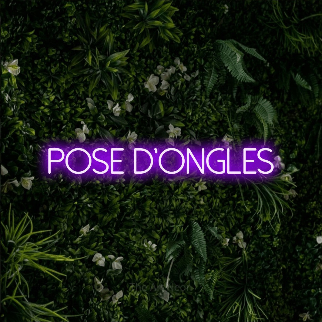 “Pose d'ongles” LED neon sign in purple, with thin sans-serif lettering, shown against a dense green plant wall.