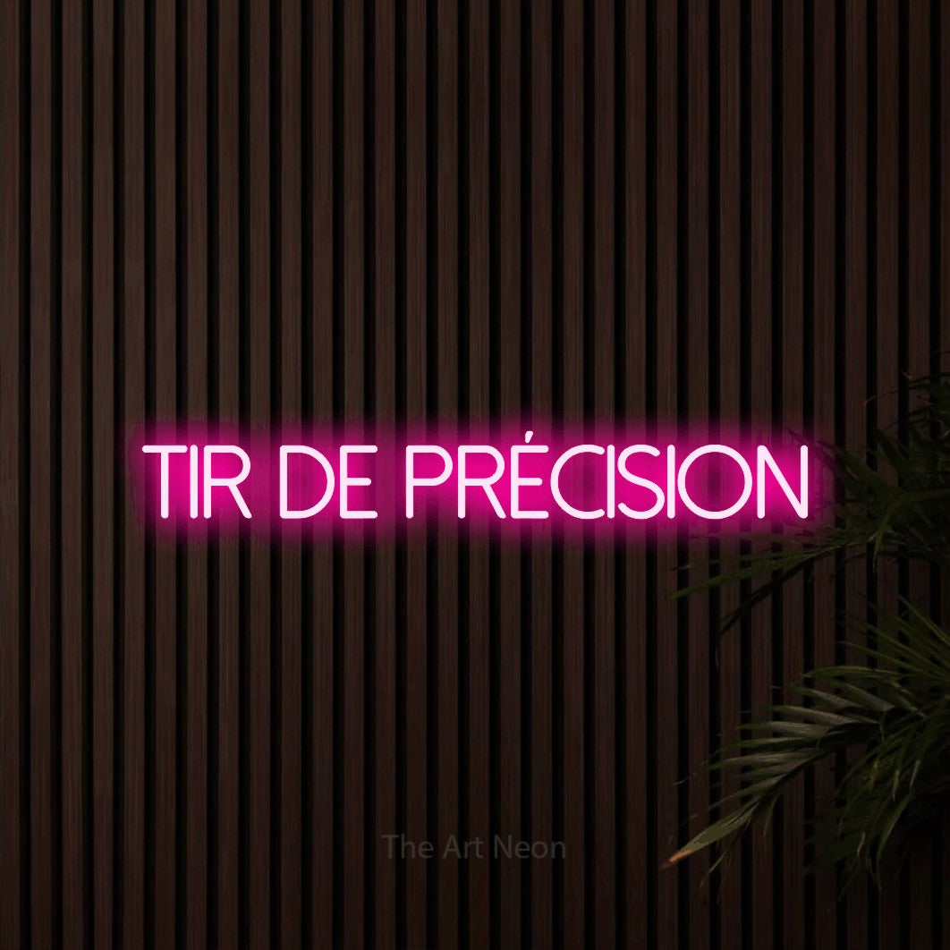 “Tir de précision” LED neon sign in hot pink, with thin sans-serif lettering, shown against dark wooden wall slats.