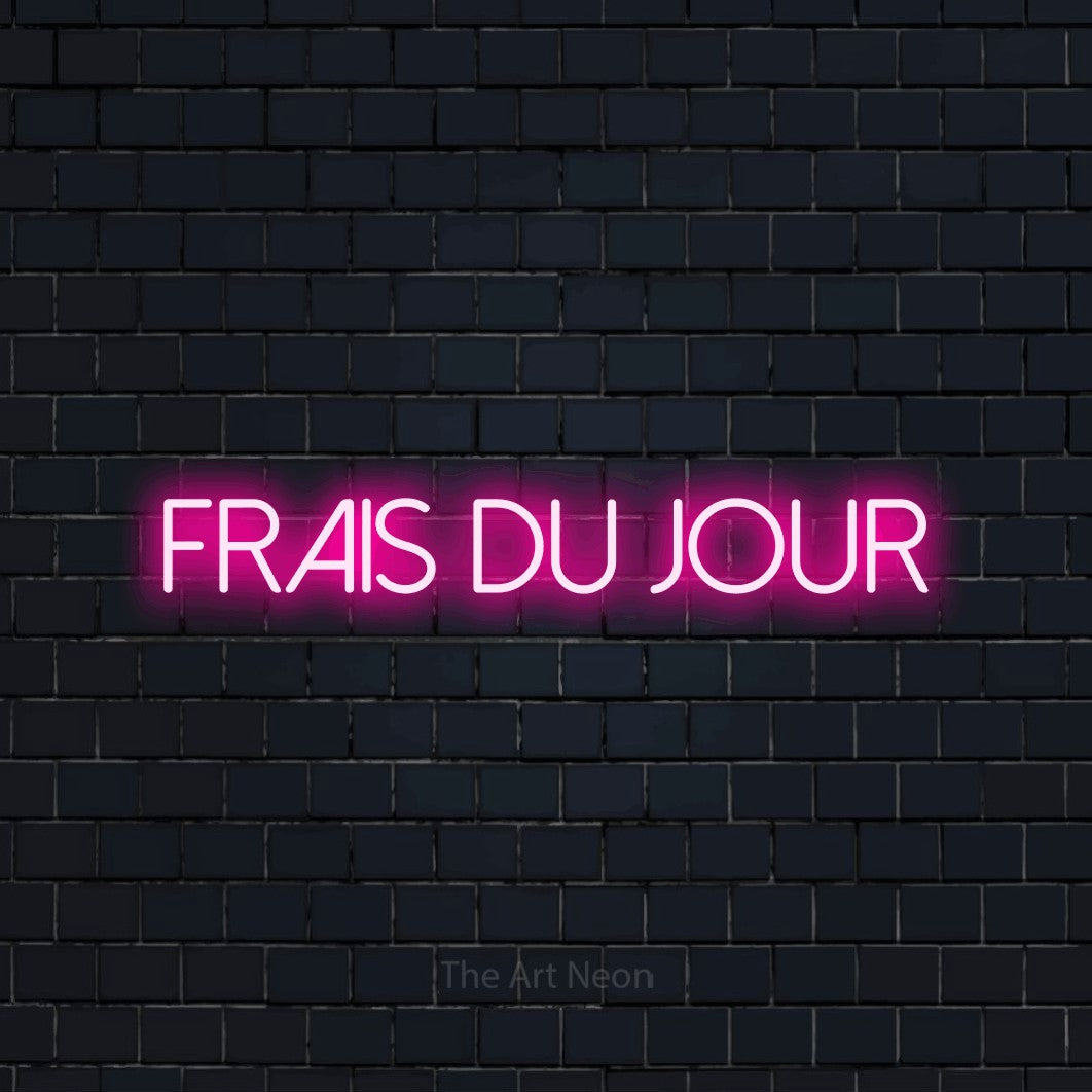 “Frais du jour” LED neon sign in hot pink, with thin sans-serif lettering, shown against a dark navy brick wall.