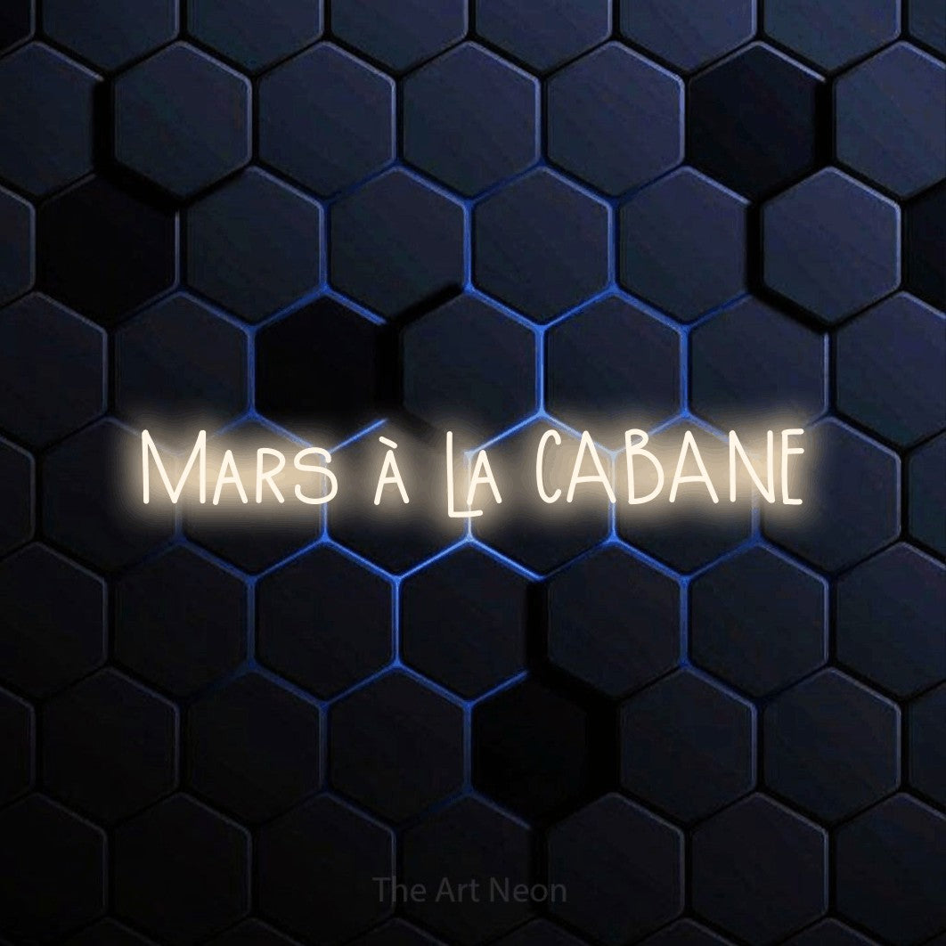 “Mars à la cabane” LED neon sign in warm white, with narrow hand-drawn lettering, shown against a dark blue honeycomb pattern.