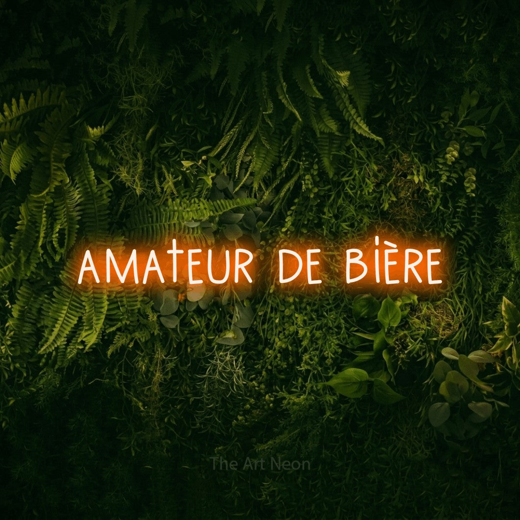 “Amateur de bière” LED neon sign in orange, with narrow hand-drawn lettering, shown against a dark moss and forest backdrop.