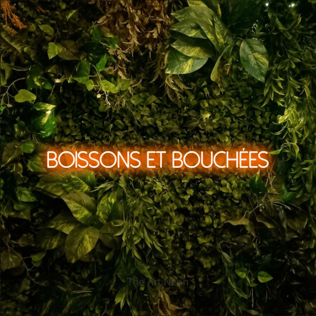 Enseigne néon LED « Boissons et bouchées » en orange, en lettres fines sans empattement, présentée sur un feuillage vert et jaune vif, pour un bar ou un pub.