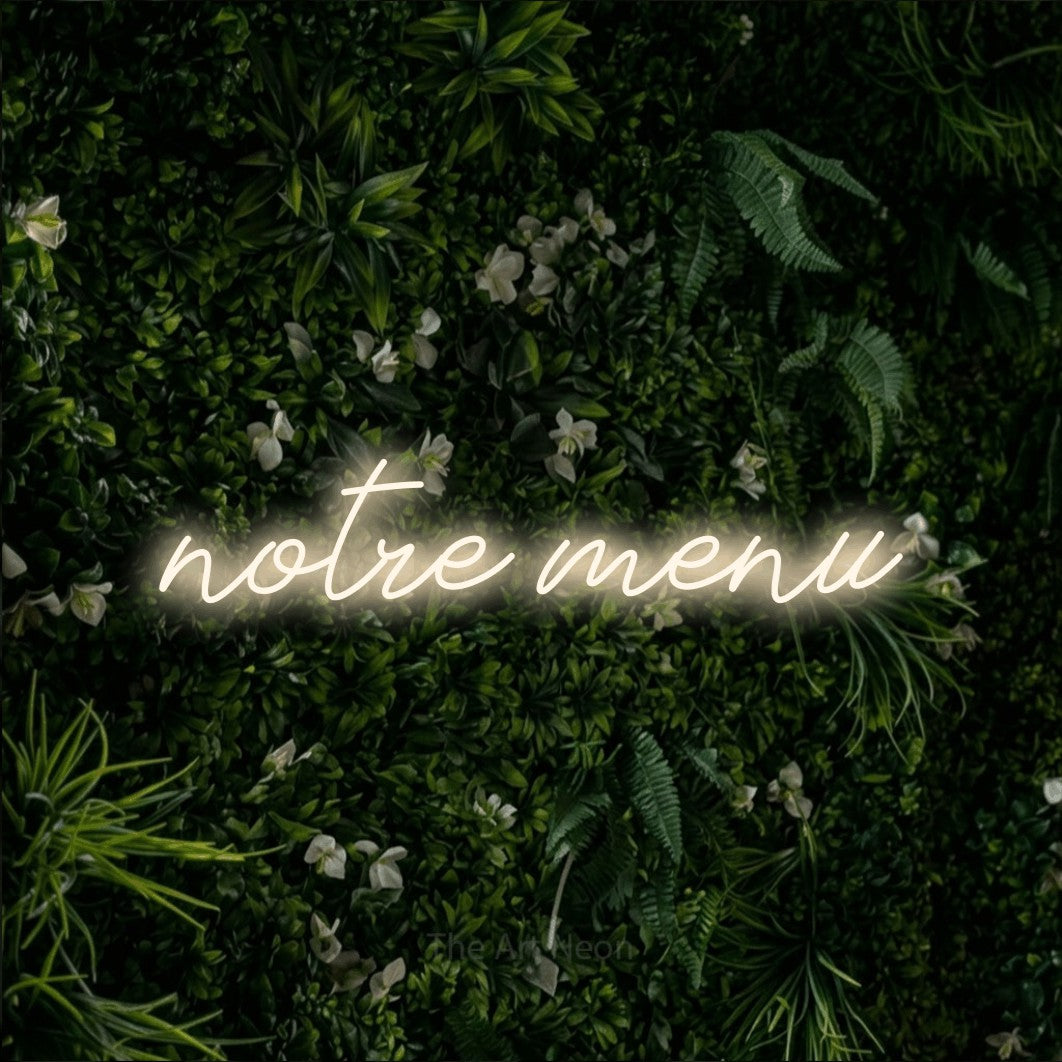 “Notre menu” LED neon sign in warm white, with cursive lettering, shown against a dense green plant wall.