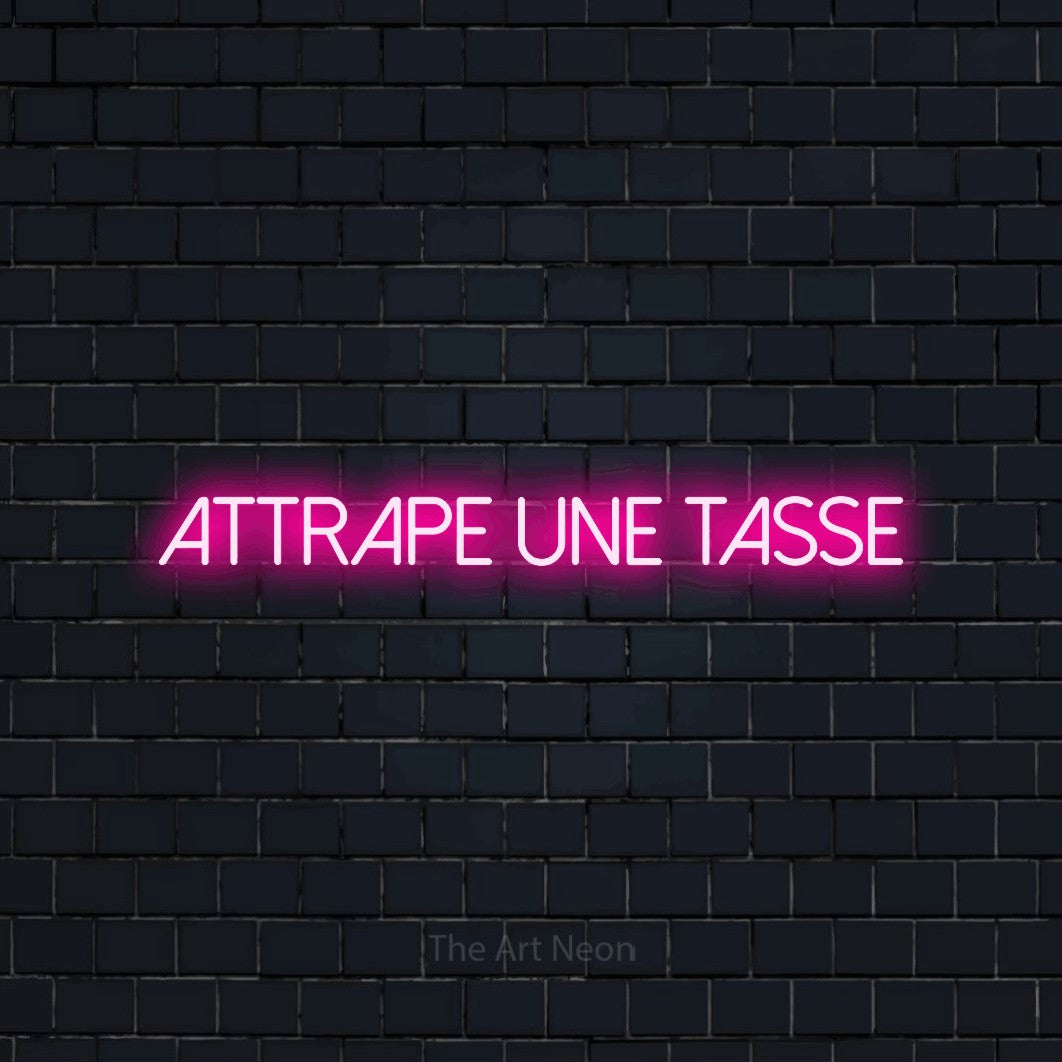 “Attrape une tasse” LED neon sign in hot pink, with thin sans-serif lettering, shown against a dark navy brick wall.