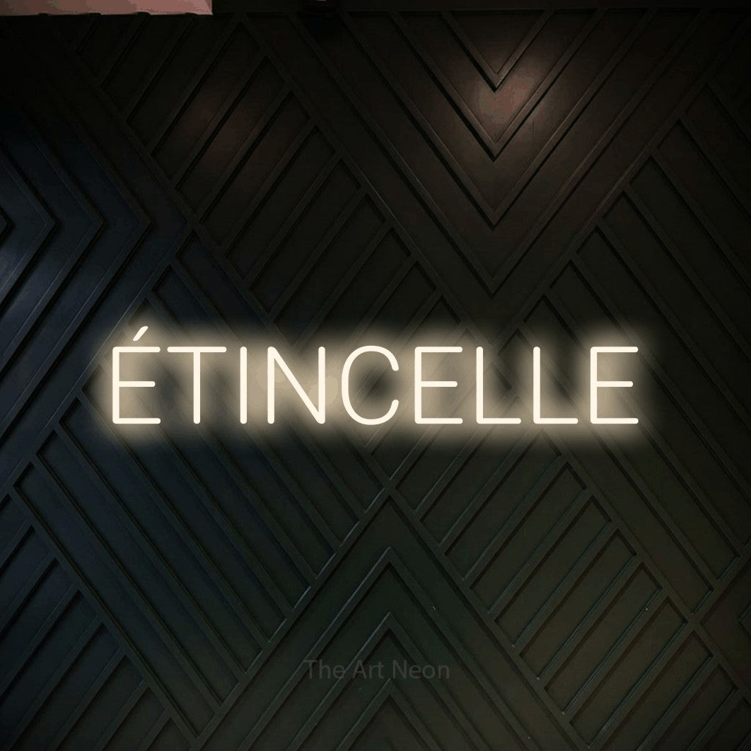 “Étincelle” LED neon sign in warm white, with rounded sans-serif lettering, shown against a black chevron-patterned wood wall.