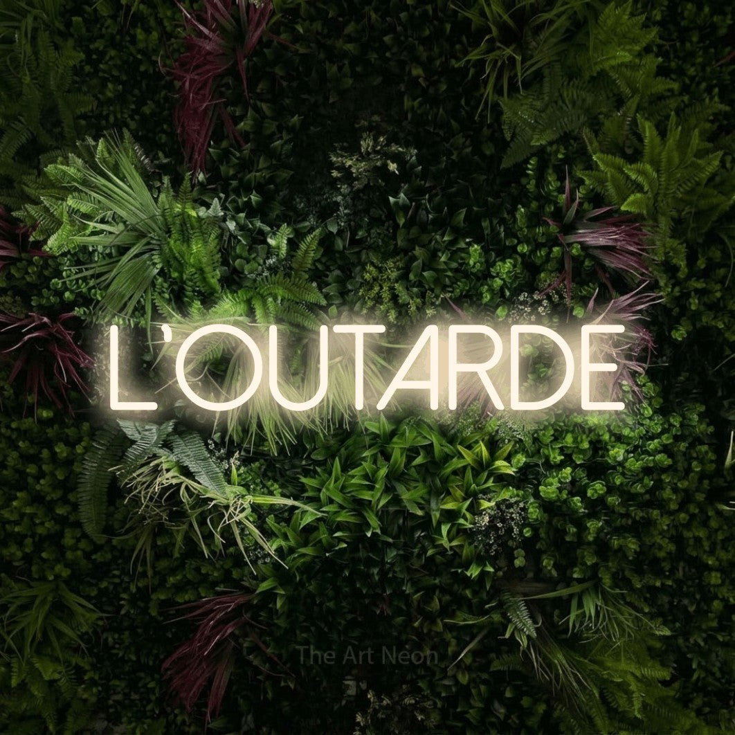 Lettrage en néon LED « L'outarde » en blanc chaud, en lettres fines sans empattement, présenté sur un mur végétal aux fleurs roses, pour un décor canadien.