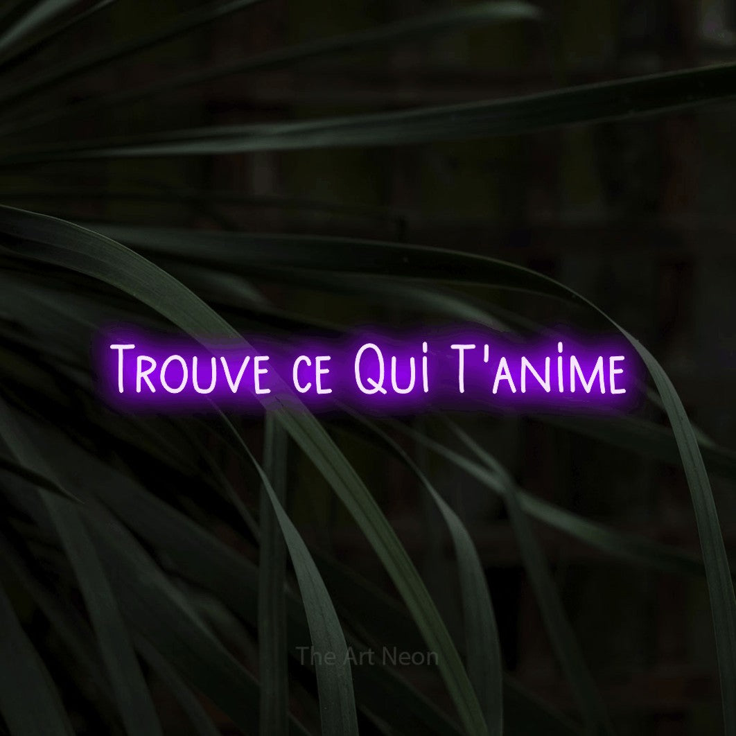 “Trouve ce qui t'anime” LED neon sign in purple, with narrow hand-drawn lettering, shown against a close-up of dark foliage.