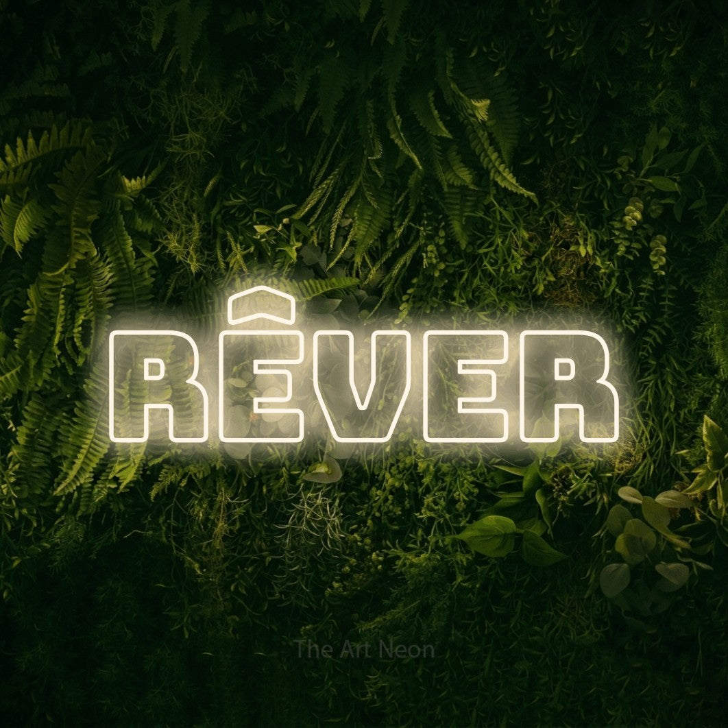 “Rêver” LED neon sign in warm white, with bold outline lettering, shown against a dark moss and forest backdrop.