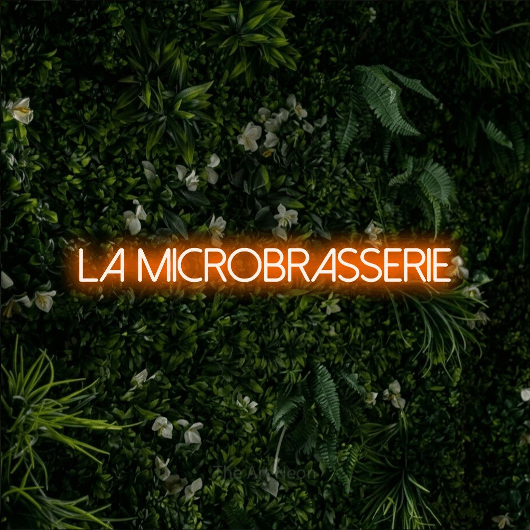 “La microbrasserie” LED neon sign in orange, with thin sans-serif lettering, shown against a dense green plant wall.