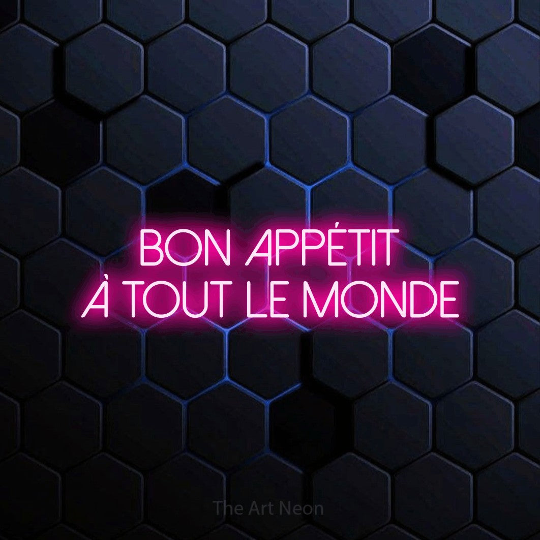 “Bon appétit à tout le monde” LED neon sign in hot pink, with thin sans-serif lettering across 2 lines, shown against a dark blue honeycomb pattern.