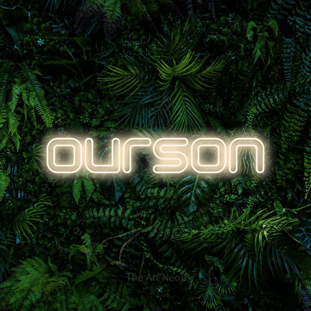“Ourson” LED neon sign in warm white, with futuristic double-line lettering, shown against dense tropical foliage.