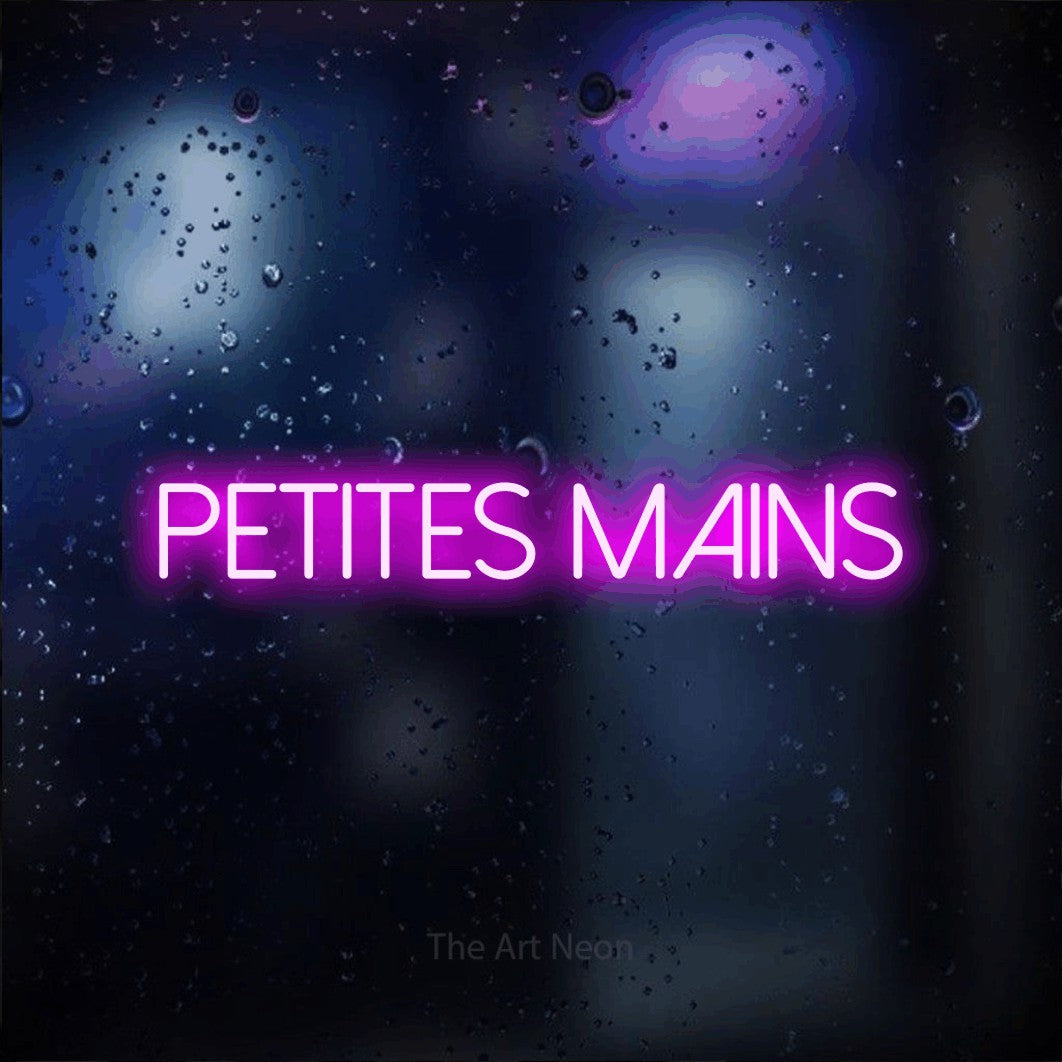 “Petites mains” LED neon sign in pink, with thin sans-serif lettering, shown against glass with blue and purple reflections.