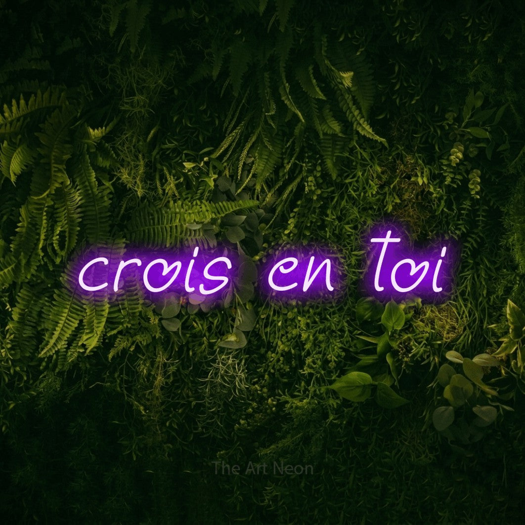“Crois en toi” LED neon sign in purple, with slanted handwritten lettering, shown against a dark moss and forest backdrop.