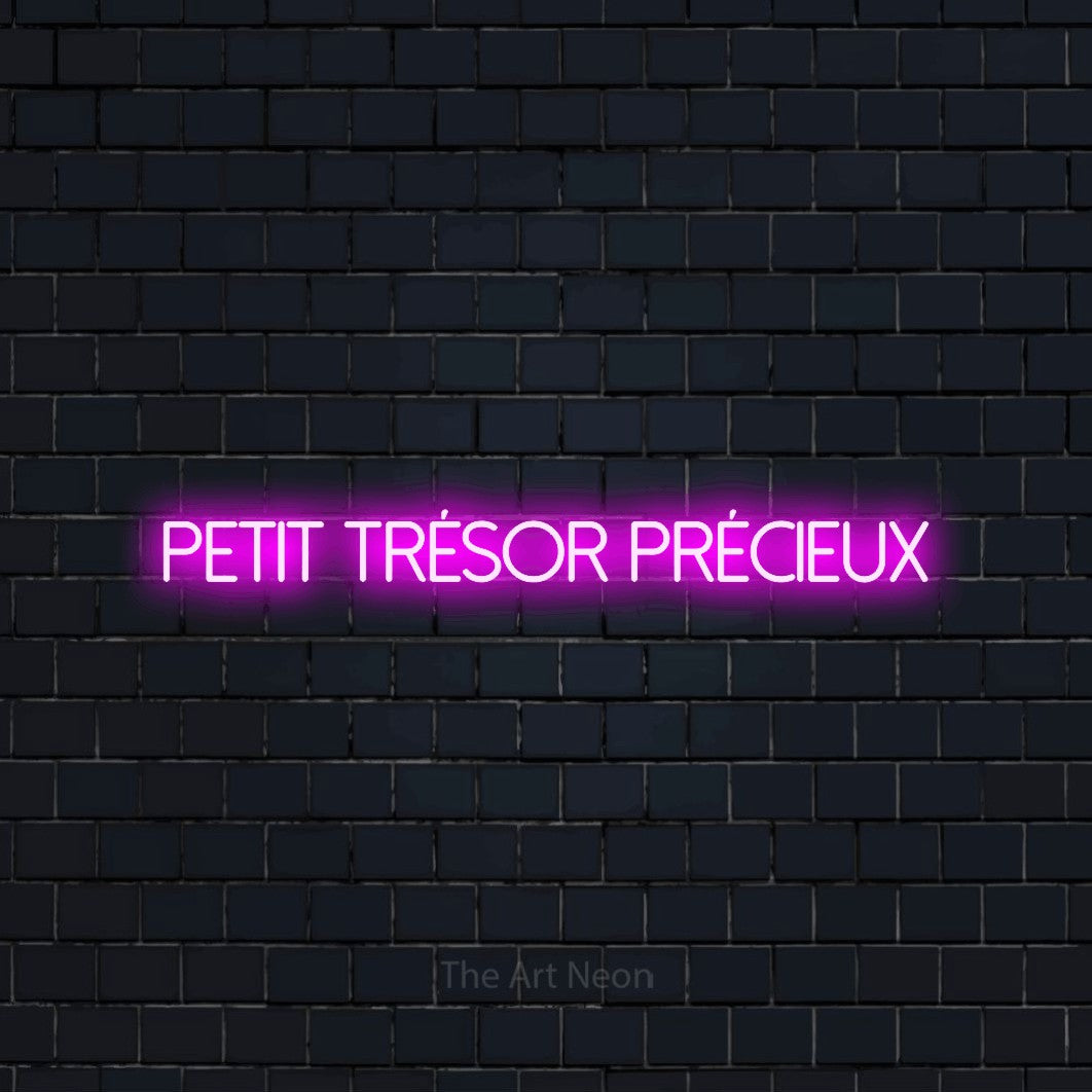 Néon LED « Petit trésor précieux » en rose, en lettres fines sans empattement, mis en scène sur un mur de briques bleu marine foncé, pour une fête prénatale.