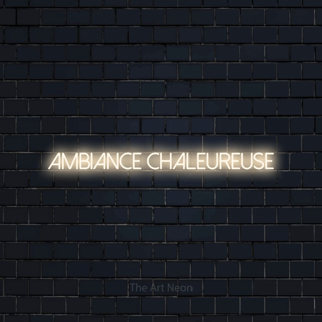 “Ambiance chaleureuse” LED neon sign in warm white, with thin sans-serif lettering, shown against a dark navy brick wall.
