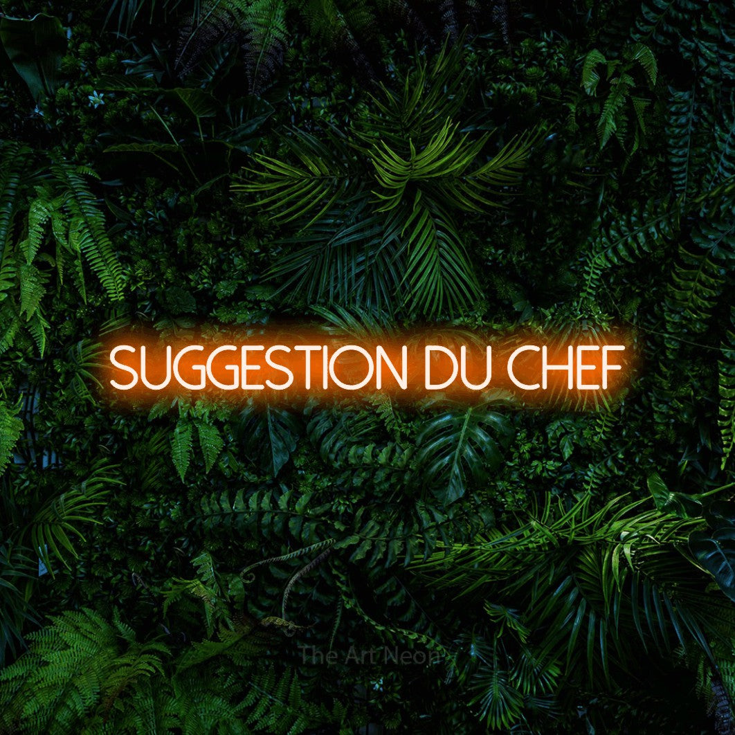 “Suggestion du chef” LED neon sign in orange, with thin sans-serif lettering, shown against dense tropical foliage.