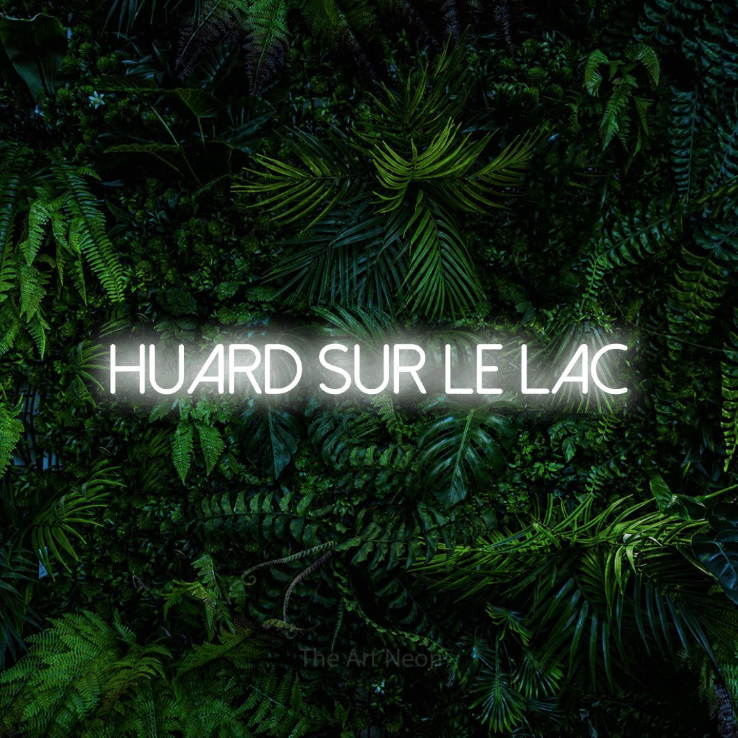 Aperçu d’une enseigne néon LED « Huard sur le lac » en blanc froid, en lettres fines sans empattement, photographiée devant un feuillage tropical dense, pour un décor canadien.